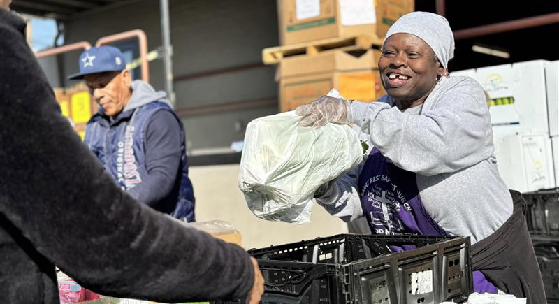 A woman smiles as she hands over a bag of groceries to a man