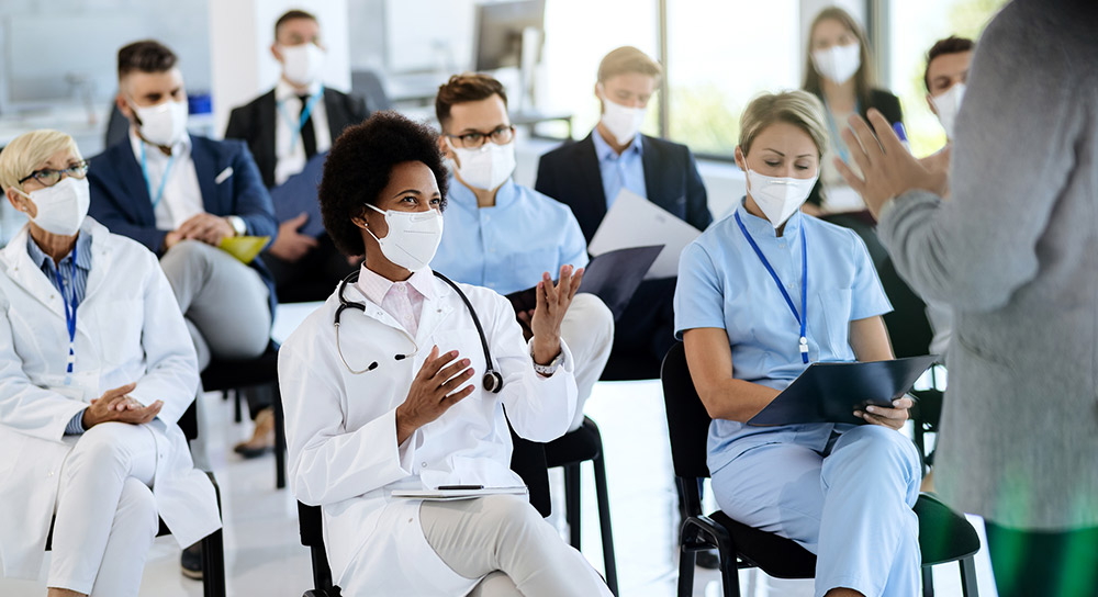 A group of masked healthcare workers sit in a classroom setting