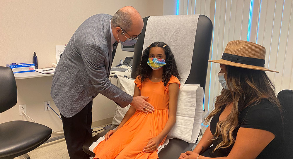 A tween-aged girl is examined by a male doctor as her mother sits nearby