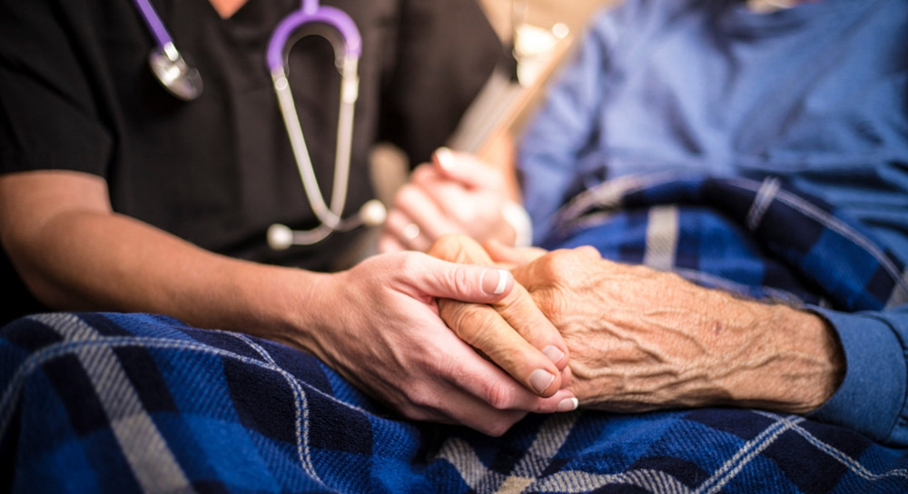 close up of a home health nurse grasping the hands of an elderly patient