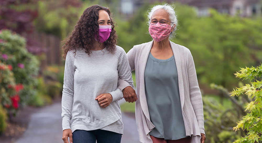 An young woman and an older woman walk outside with linked arms