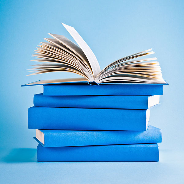 600x600_Books A stack of books with blue spines on a blue background. The top book is open with pages fanned upward