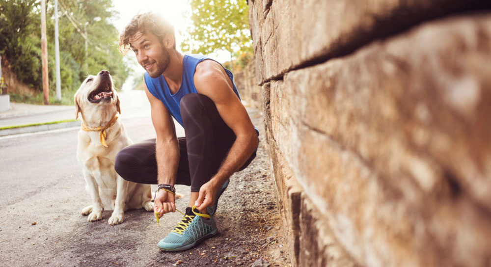 A man kneels down to tie his show while a golden retriever looks on
