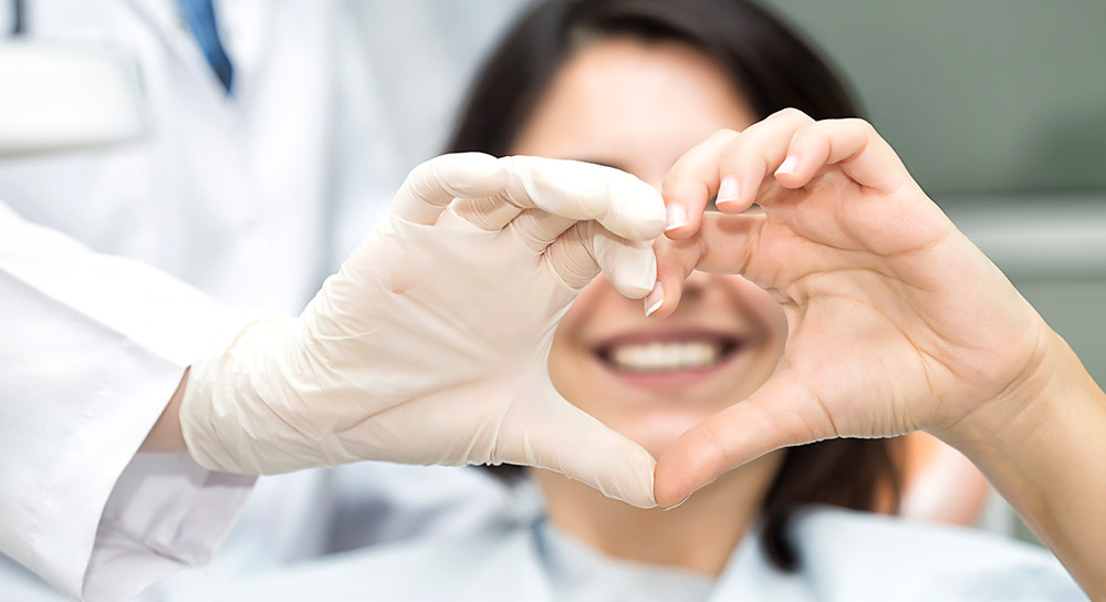 A gloved hand and an ungloved hand form a heart with their fiingers