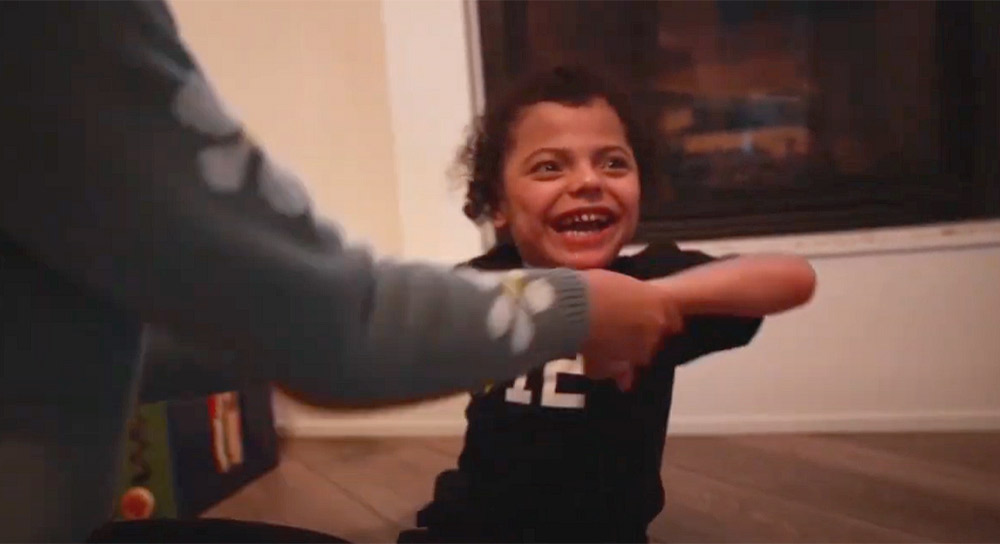 Toddler Troy Fuentes is held by his hands as he looks off into the distance and smiles. 