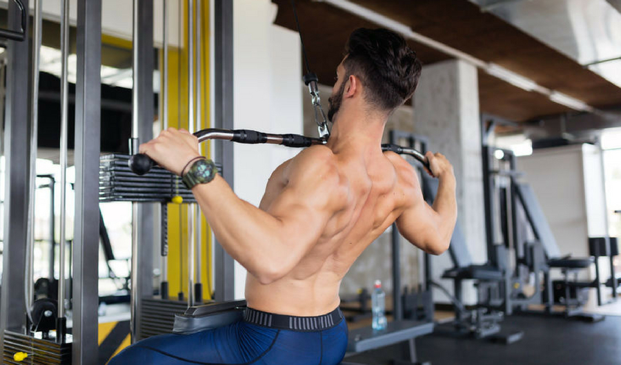 A man's back is shown as he uses gym equipment to do a lat pulldown