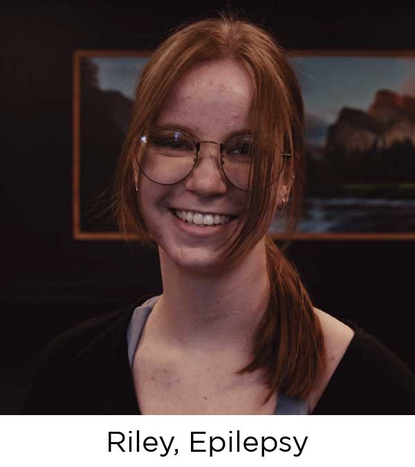 Young woman with red hair and glasses smiles at the camera