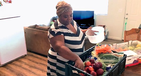 woman grabbing fresh vegetables out of plastic milk crate