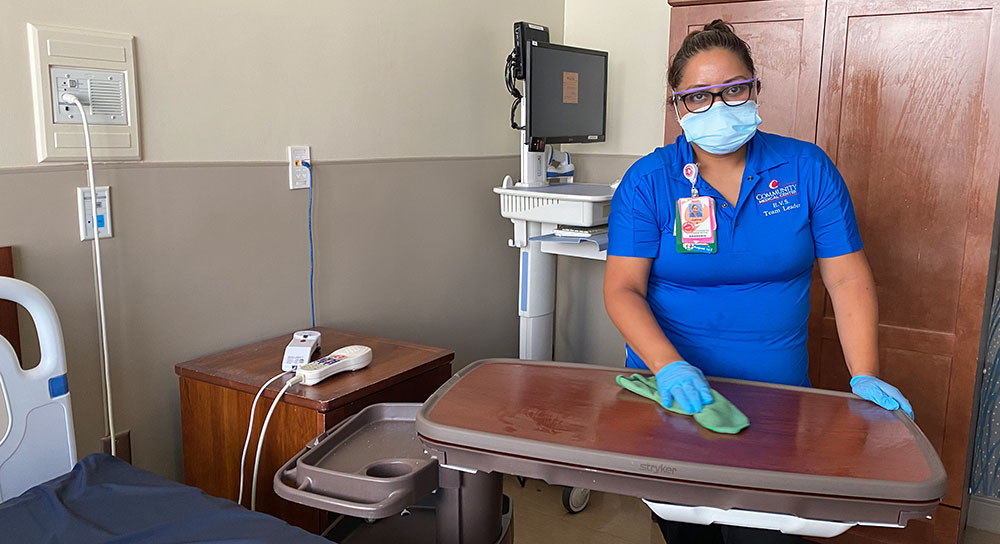 A woman in a mask cleans a table in a hospital room