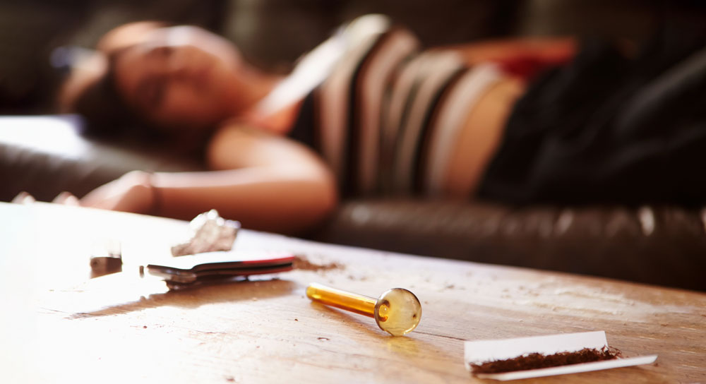 Close up of drug paraphernalia with a woman passed out in background