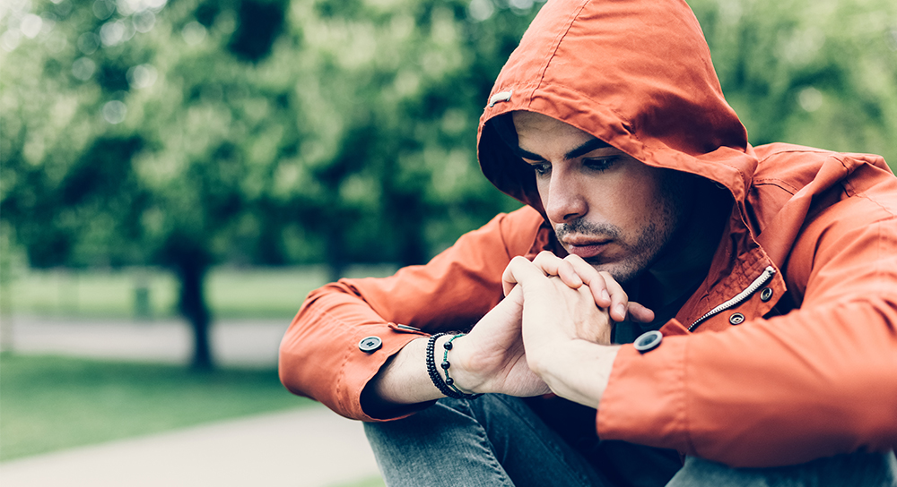 man in orange jacket has hands clasped together while deep in thought
