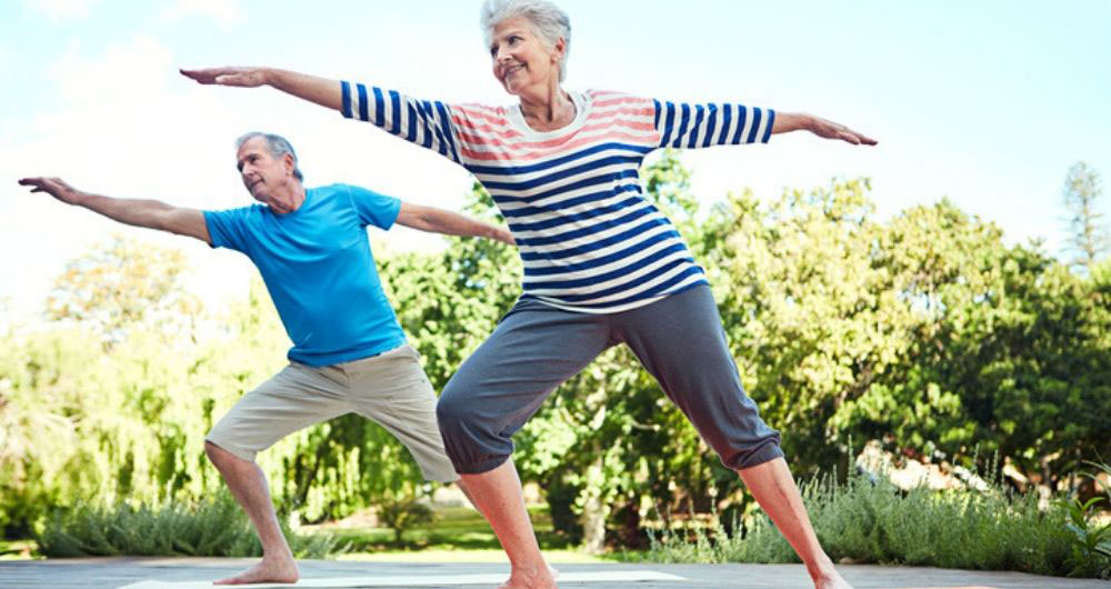 Two senior adults practice yoga outside