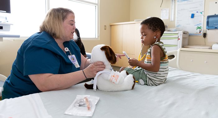 Child-Life-Play-Stuffed-Animal Child Life Specialist distracts a toddler with a stuffed animal and a stethoscope