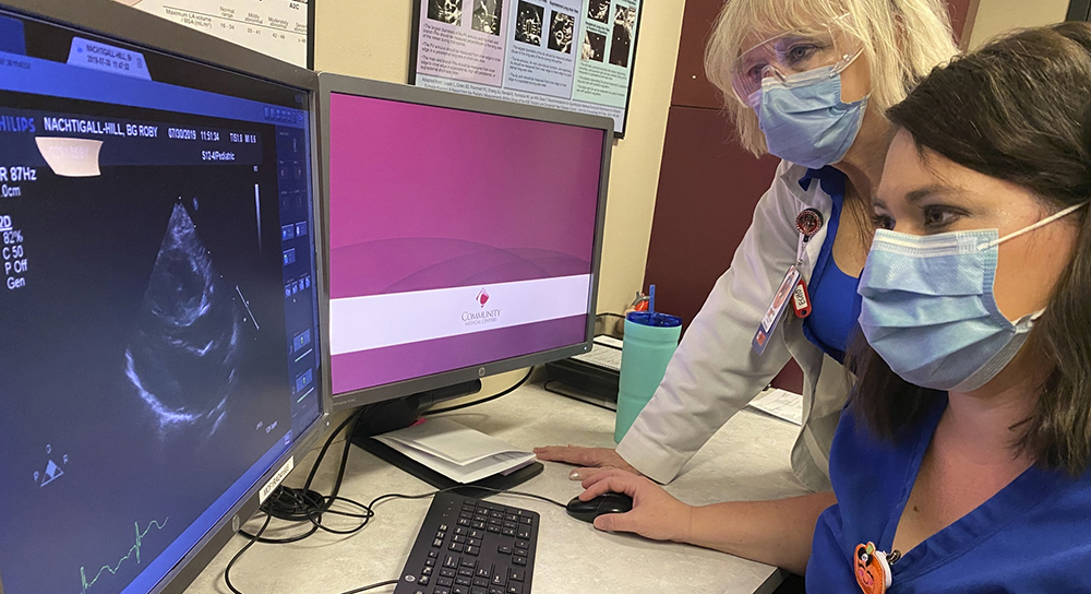 Two masked women look at an X-ray image on a screen