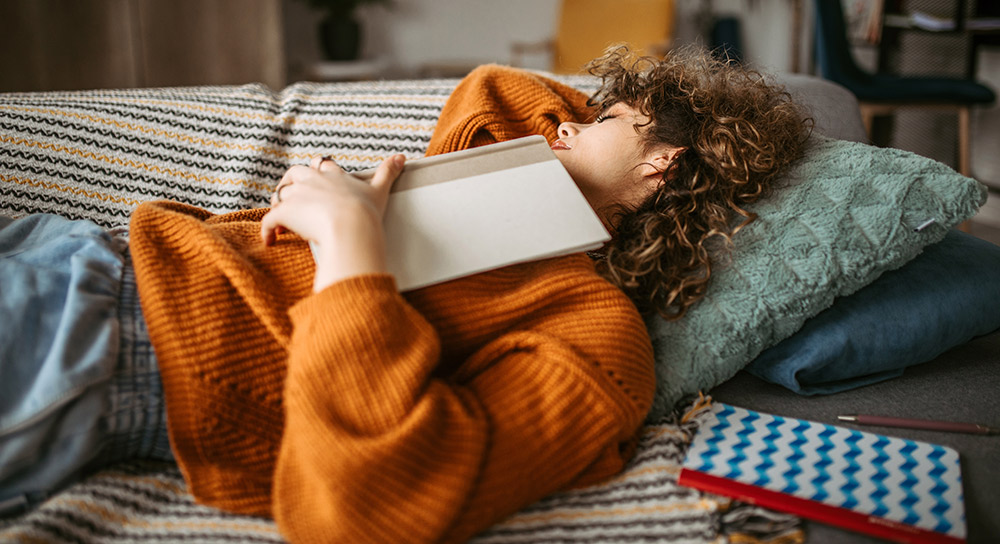 A woman sleeps on a couch with a book on her chest