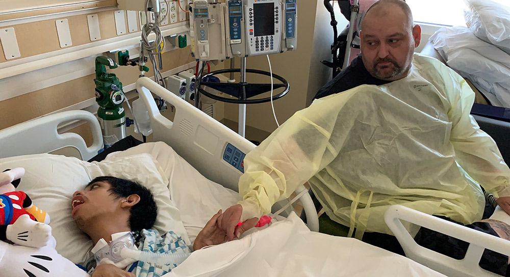 father sitting next to his son in a hospital bed at the pediatric intensive care unit during COVID