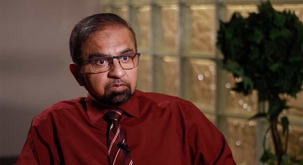 Man in a red shirt and tie is interviewed in a room