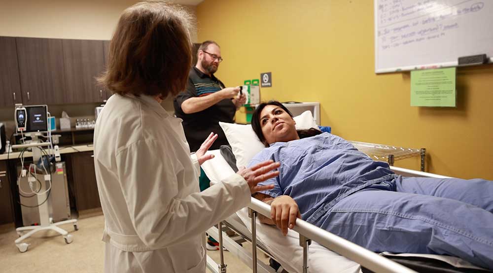 A female patient in a hospital bed looks up at her female doctor, who is preparing her for hyperbaric oxygen treatment