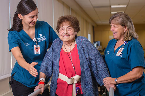 CRMC-Rehab-Patient-Walking-Caregivers A mature woman is being aided in using her walker by two female healthcare workers