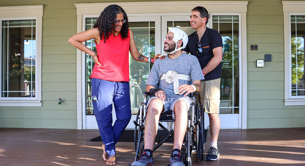 women standing with her hand on the shoulder of a man wearing a helmet in a wheelchair
