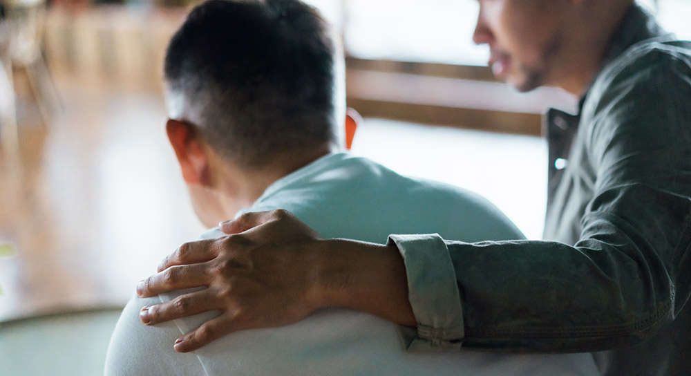 A comforting hand is placed on the back of a man