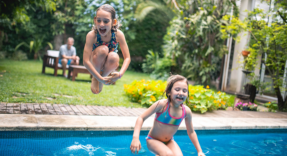 Two young girls jump into a swimming pool