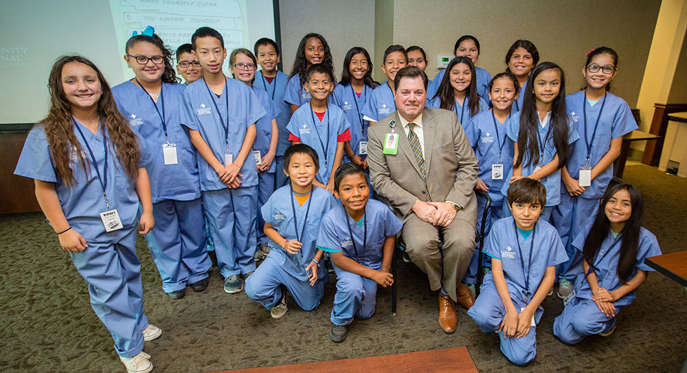 Community CEO Craig Wagoner is surrounded by a group of smiling Birney Elementary schoolkids in hospital scrubs