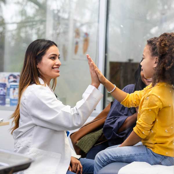 600x600_Peds-Doctor A young Latina doctor high fives her patient, a Black tween girl in a yellow shirt