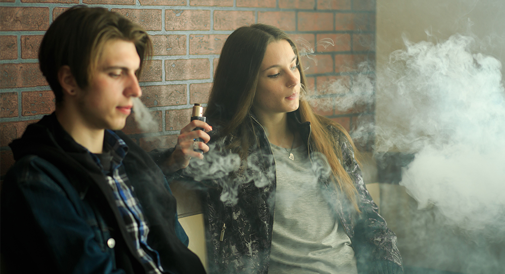 Two teens are shown vaping in a cloud of smoke