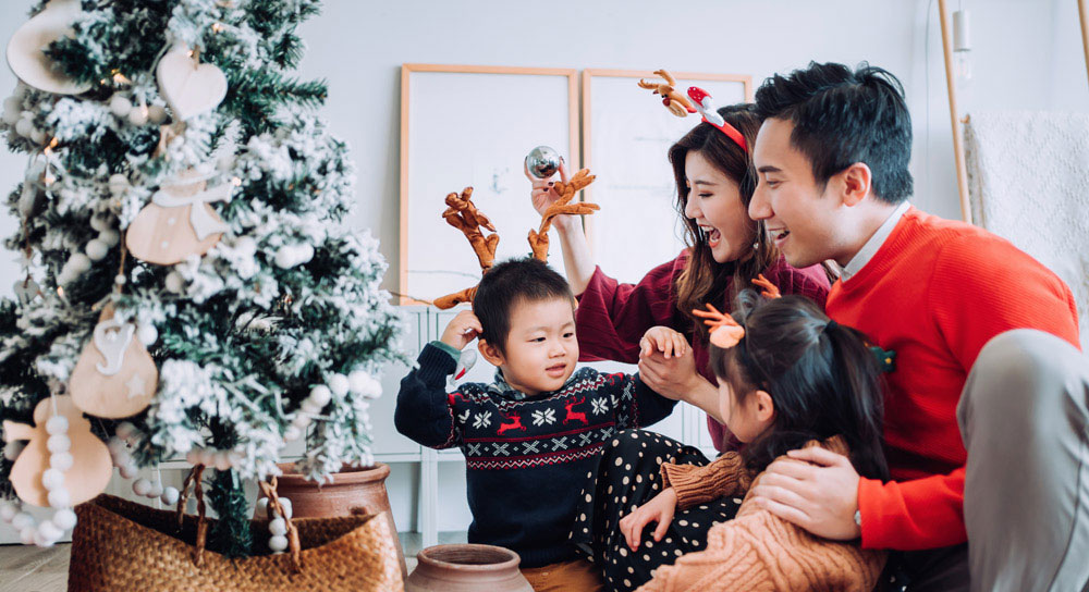 A family -- mom, dad and two children -- gather in front of the Christmas tree. 