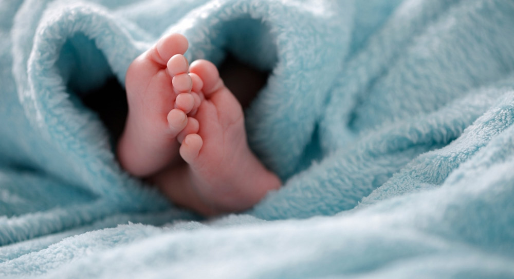 A small pair of newborn feet peek out from a light blue baby blanket