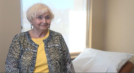 Theodora Clifford, white woman in a yellow shirt and animal print jacket, sits in an exam room